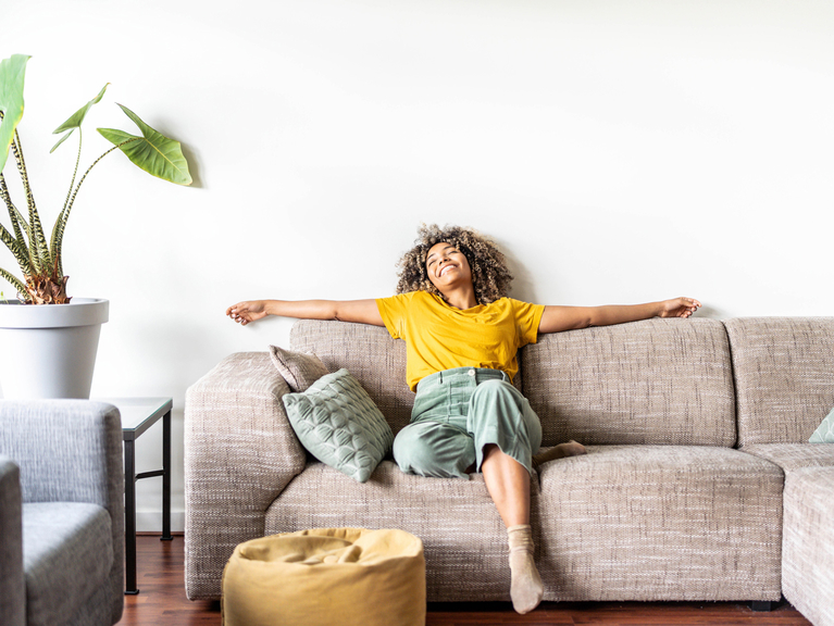 Eine lächelnde Frau, die ihre freie Zeit auf der Couch genießt und sich entspannt.