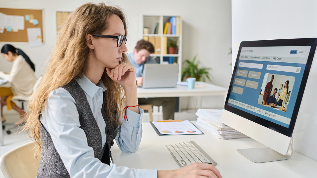 Eine junge Frau, die an ihrem Arbeitsplatz sitzt und den Computer benutzt, um nach einer neuen Stelle zu suchen.