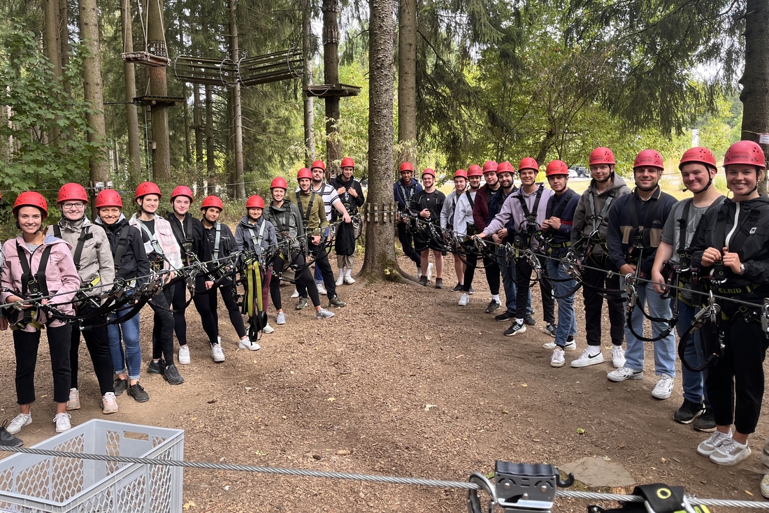 Eine Gruppe Auszubildender steht mit roten Helmen im Kletterwald.