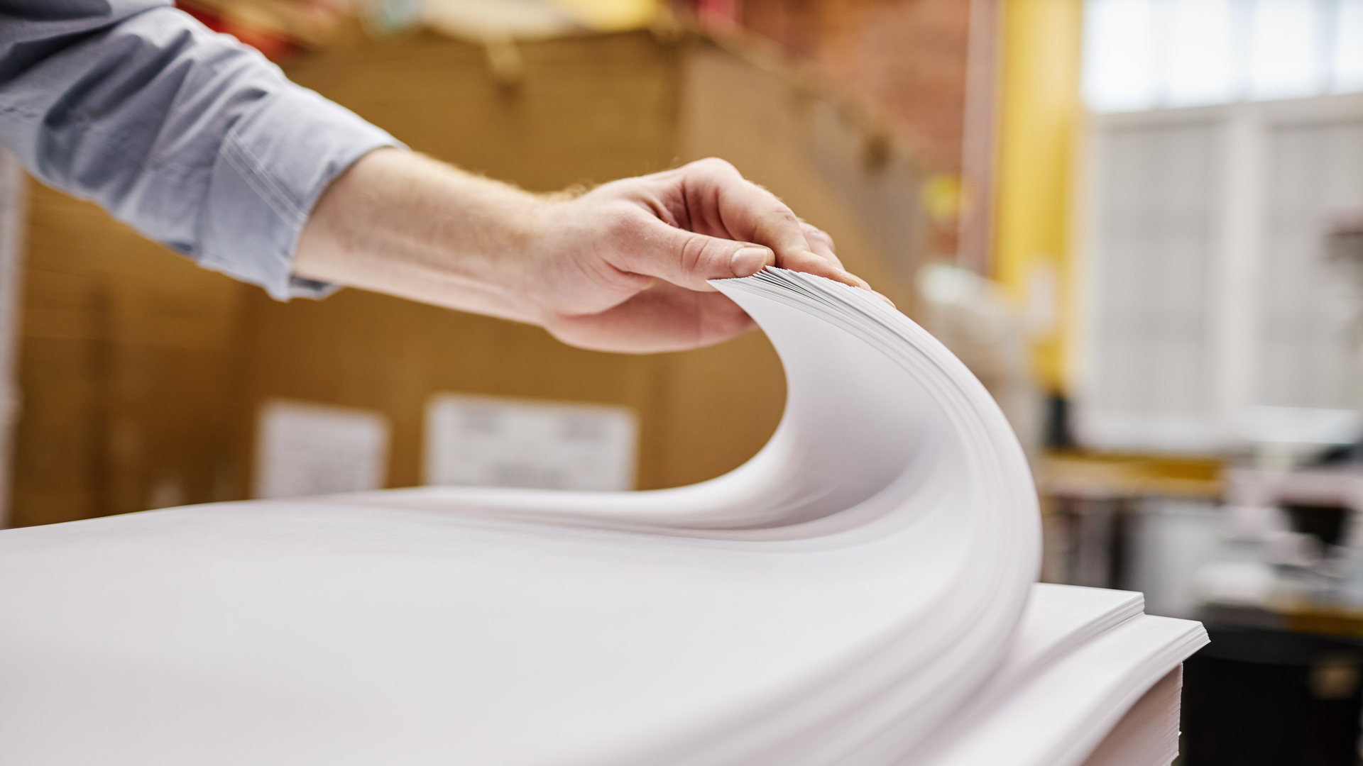 Nahaufnahme einer Person beim Anheben eines Papierstapels in einer Druckerei.